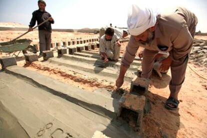 Tres voluntarios aplican cemento a las tumbas de soldados leales a Muammar Gaddafi que han sido enterrados en un cementerio de Misrata.