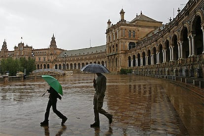 Dos turistas pasean con sus paraguas por la Plaza de España de Sevilla.