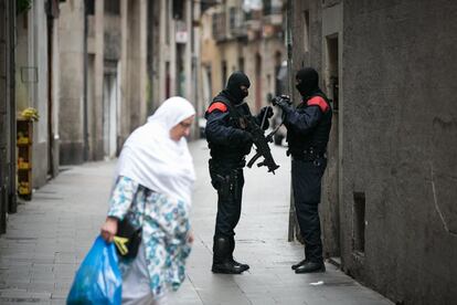 Una mujer pasa frente a dos agentes por la calle de la Cera, donde se está llevando a cabo parte de la operación de los 'mossos' contra los narcopisos.