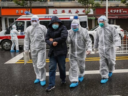 Tres médicos, de blanco, acompañan a un paciente enfermo al hospital de Wuhan, en China.