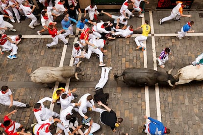 Varios corredores caen al suelo al paso de los toros de la ganadería de José Escolar, durante el séptimo encierro este sábado en Pamplona. 