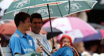 Djokovic, con el recogepelotas al que quitó el paraguas para resguardarle de la lluvia.
