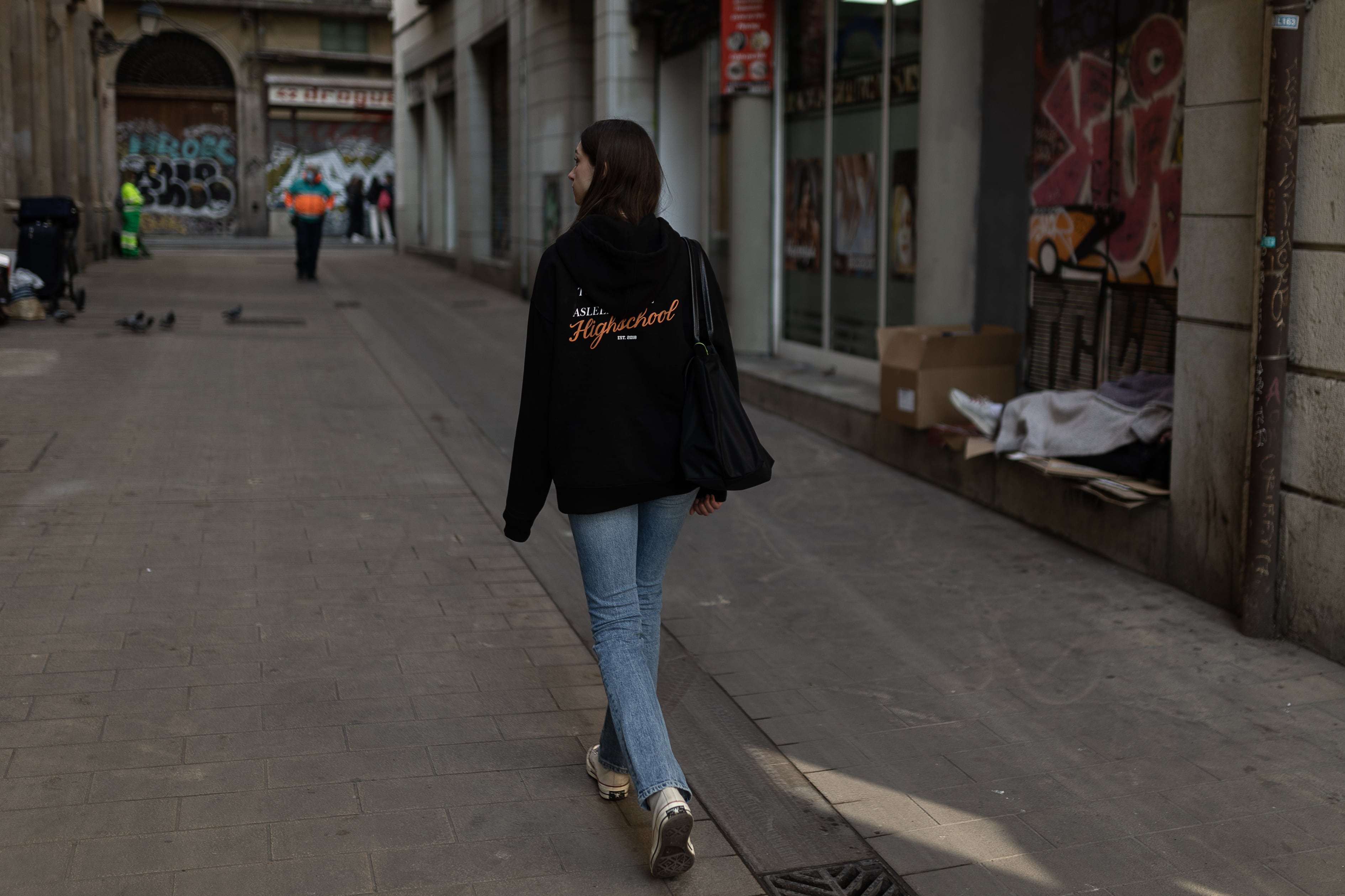 Una joven pasea por el centro de Barcelona ante una persona sin hogar.