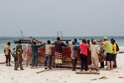 Un turista ayuda a unos pescadores de Uroa a sumergir una enorme barcaza de pesca en el mar.