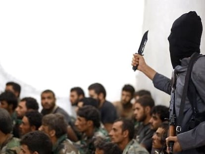 Un miembro del Estado Isl&aacute;mico sostiene un cuchillo junto a un grupo de soldados sirios capturados en Raqqa.
