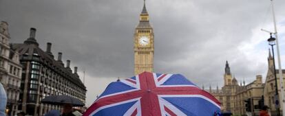 Una persona con un paraguas con la bandera de Reino Unido, delante del parlamento británico.