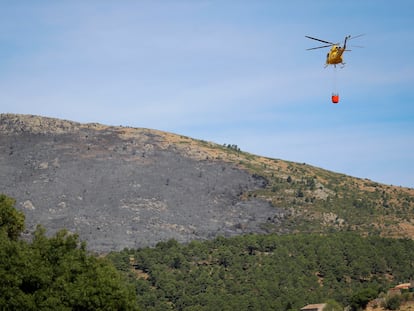 Un helicóptero transporta agua para vertirla sobre el incendio forestal originado en el término municipal de Robledo de Chavela.