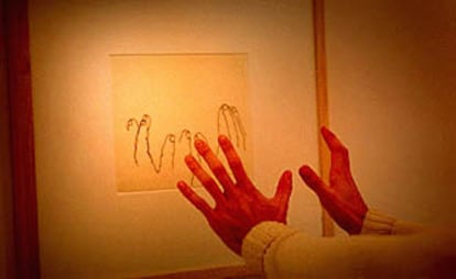 Un asistente a la exposición extiende sus manos hacia una obra de Chillida.
