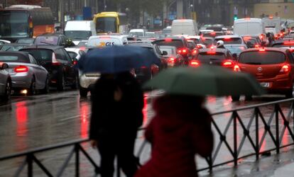 Transeúntes pasan una zona de tráfico mientras se resguardan de la lluvia bajo paraguas.