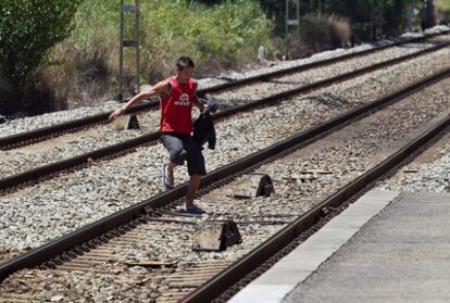 Un joven atraviesa las vías del tren en Castelldefels para colarse y no perder un tren que espera en el andén.