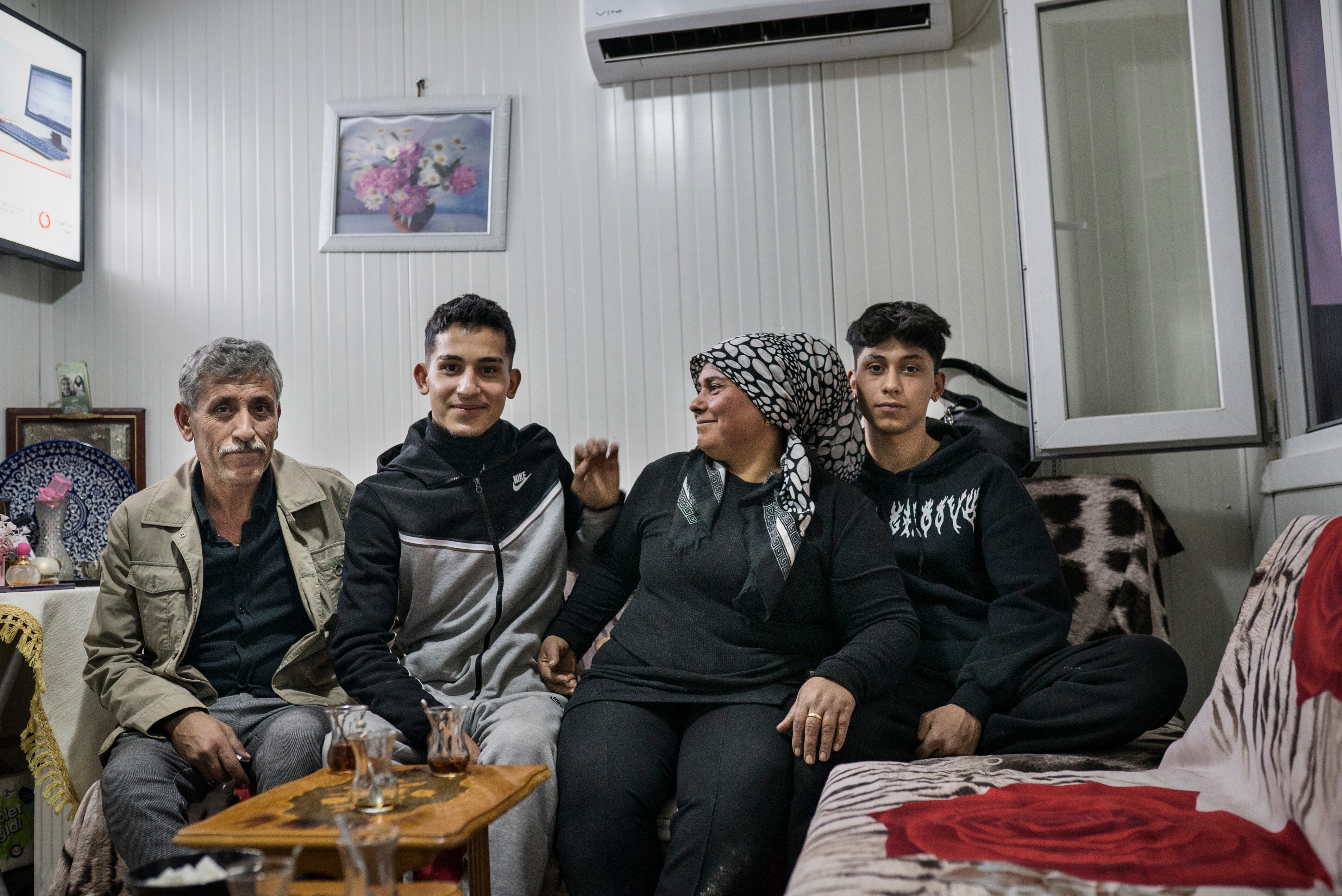 La señora Aziza, sus dos hijos y un pariente en el pequeño contenedor de obra dentro del campamento para damnificados en el que reside, en la ciudad de Antioquía (sur de Turquía). Aziza, que trabaja vendiendo verduras en el mercado, perdió tres hijos, dos nietos y a su nuera en el terremoto.  