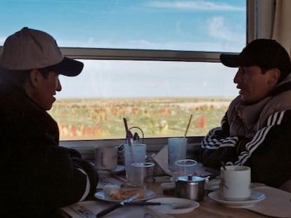 Dos bolivianos conversan en uno de los trenes que atraviesa el altiplano, con campos de quinua coloreándose al fondo.