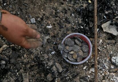 Una mujer recoge monedas carbonizadas —pertenecientes a su hija— entre los escombros de su casa.