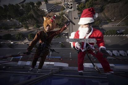 Un par de limpiacristales disfrazados de Santa Claus y de reno posan para una fotografía mientras limpian las ventanas del Centro Comercial Daiba, de Tokio (Japón).