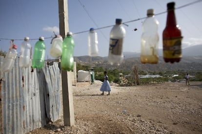 Botellas de plástico vacías cuelgan en el exterior del puesto de un vendedor de bebidas en Canaán, Haití. Mientras que algunos ven signos alentadores deautosuficiencia en esta localidad, otros ven males familiares para los habitantes de la nación más pobre de América: servicios públicos inexistentes, escasez de trabajos dignos y condiciones de vida insalubres.