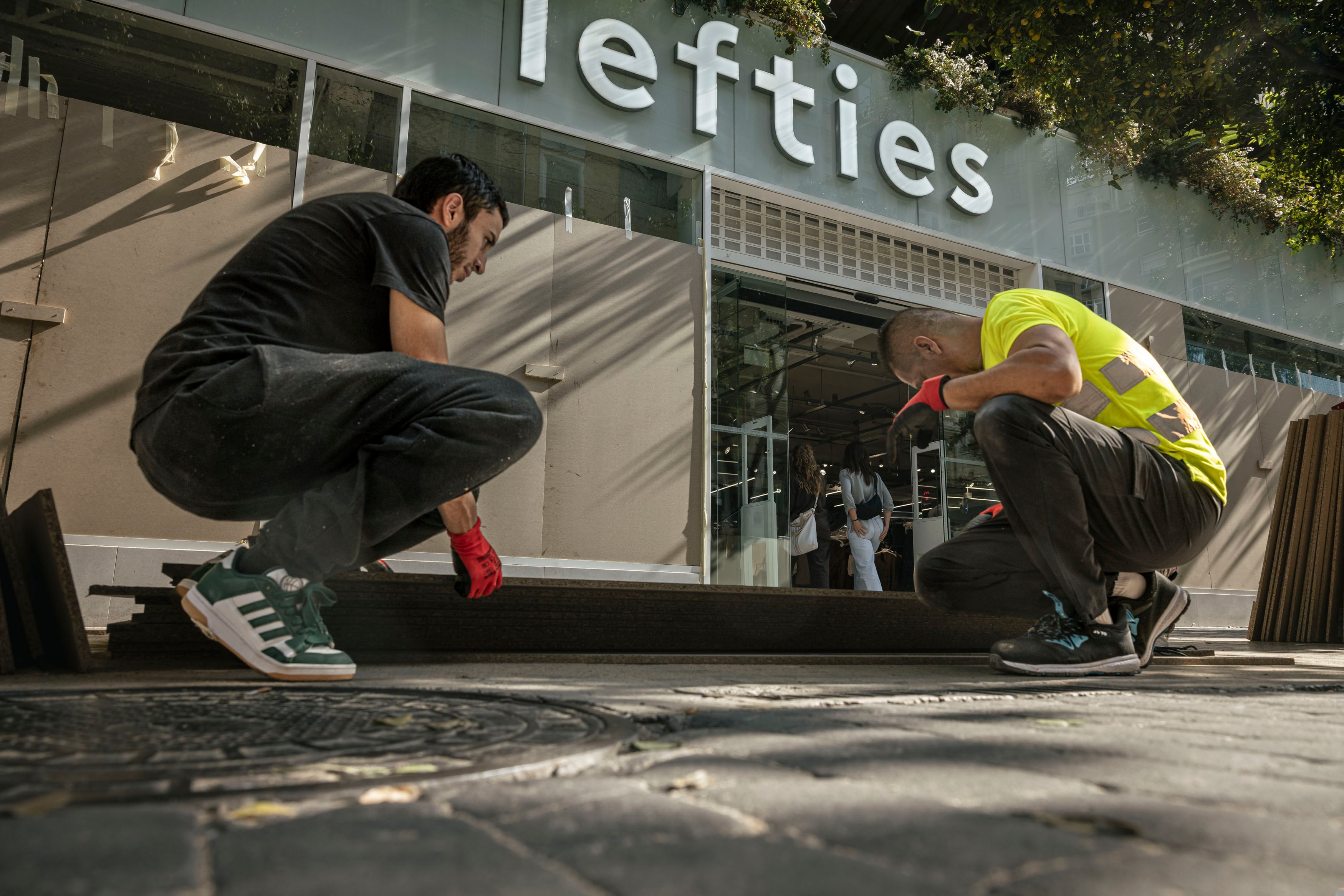 Un equipo de trabajadores instala protecciones temporales en la fachada de un comercio del centro de Valencia ante la previsión de posibles actos vandálicos durante la jornada del sábado.