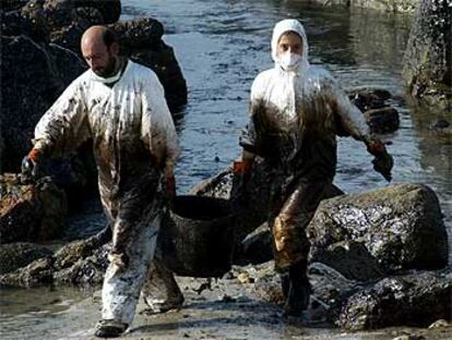 Dos voluntarios cargan los restos de fuel vertido por el <b><i>Prestige</b></i> en la playa de Muxía, en A Coruña.