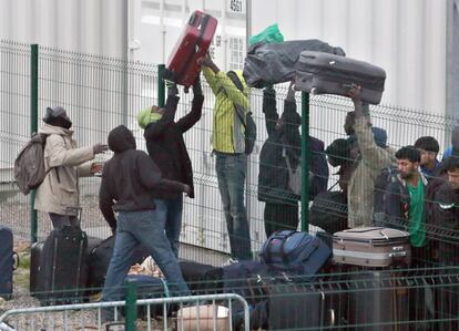 Un grupo de migrantes ayudan a dejar algunas maletas tras las vallas antes de abandonar el campamento de Calais (Francia).