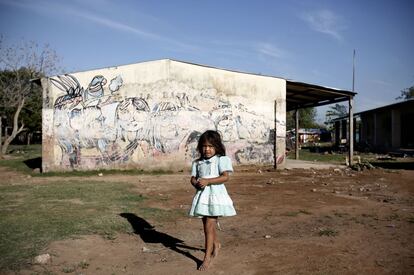 Una niña avá guaraní indígena camina por la comunidad de Cerro Poty, situada situada junto al vertedero de Asunción. Allí decenas de familias indígenas expulsadas de sus tierras sobreviven desde hace años. En el muro del fondo puede verse un mural sobre los pueblos indígenas.