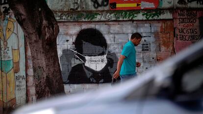 Homem caminha diante de grafite do presidente Bolsonaro, no Rio.
