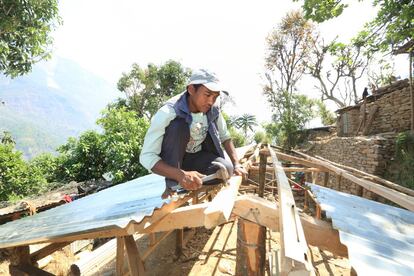Ram Kumak Kame trabaja en el techo de chapa de una de las viviendas. En Sindhupalchok, el paisaje ha cambiado: las casas de adobo y piedra son ahora pequeños diseminados que recuerdan a chabolas entre plantaciones de arroz, patata y otros vegetales.