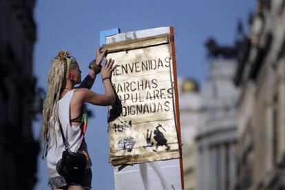Una mujer coloca un cartel de bienvenida a las marchas populares en la Puerta del Sol.