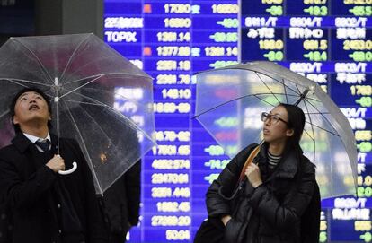 Un par de viandantes miran al cielo ante una pantalla que muestra informaci&oacute;n financiera en Tokio.