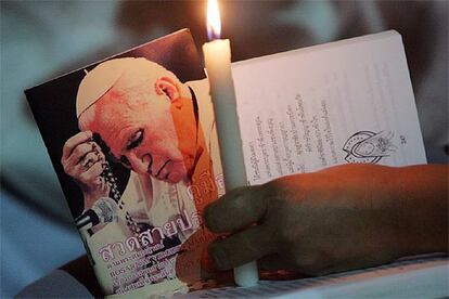 Un sacerdote sostiene una vela junto a una fotografía de Juan Pablo II durante una misa celebrada ayer en una iglesia de Phuket (Tailandia).