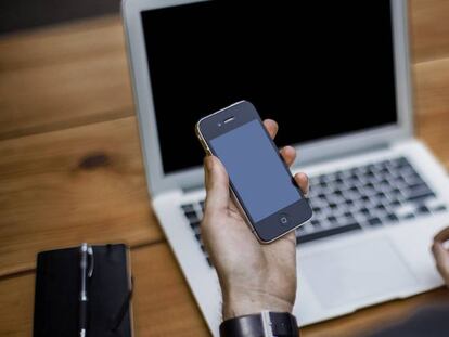 Un hombre trabaja con un teléfono móvil y un ordenador portátil.