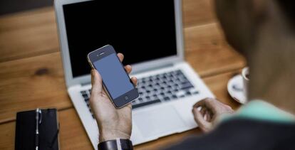 Un hombre trabaja con un teléfono móvil y un ordenador portátil.