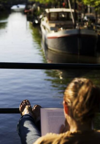 una mujer lee un libro en uno de los canales de Amsterdam.