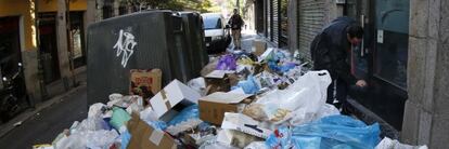 Un hombre intenta abrir un establecimiento entre una monta&ntilde;a de basura en una calle de Madrid sin determinar.