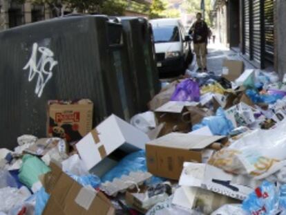Un hombre intenta abrir un establecimiento entre una monta&ntilde;a de basura en una calle de Madrid sin determinar.