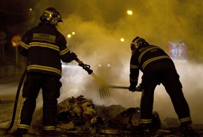 Miembros del cuerpo de bomberos, apagan uno de los muchos contenedores incendiados.