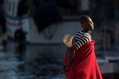 Una mujer migrante lleva un bebé a la espalda a su llegada a bordo de un guardacostas al puerto de Málaga.