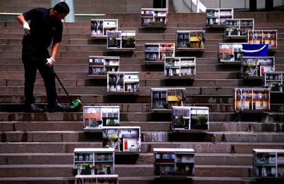 Persona limpiando los escalones de un edificio donde hay colocadas fotografias de terrazas, en el centro de Sídney (Australia).