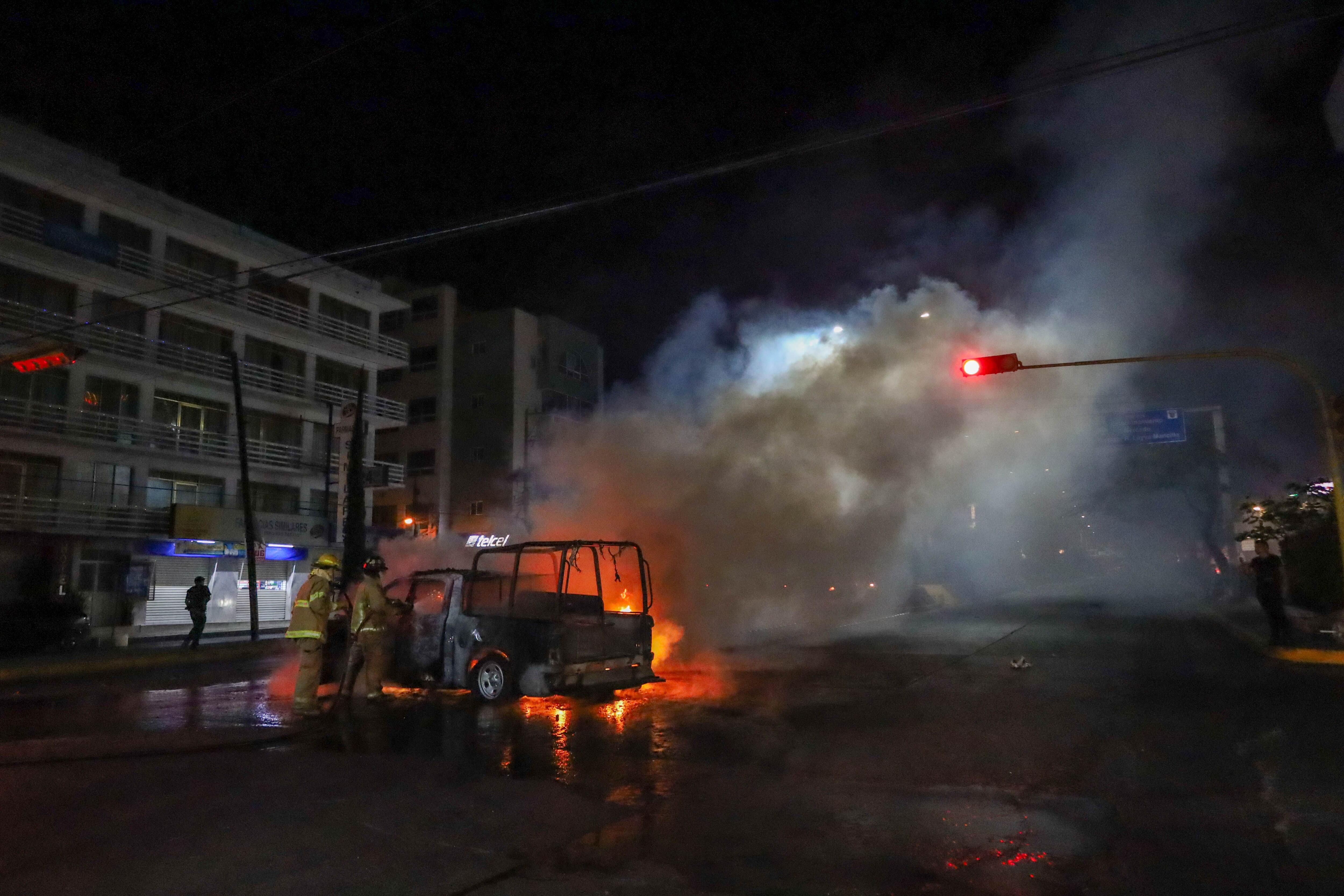 Bomberos extinguen el fuego de una patrulla incendiada por presuntos normalistas, este 8 de marzo por la madrugada, en Chilpancingo.