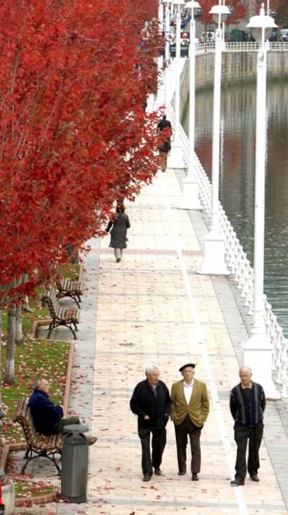 Tres jubilados pasean por la ría del Nervión, en Bilbao.