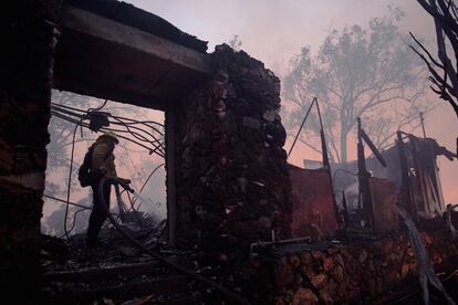 Un bombero utiliza la manguera en una casa humeante destruida por el incendio en Los Ángeles. 
