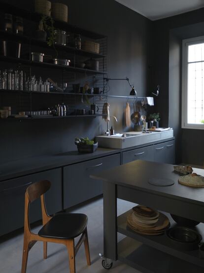 La cocina no está aislada, comparte espacio con el comedor y, al estar pintada de gris antracita, se distingue sin separarse de él. El sistema sueco de estanterías metálicas colgantes String sirve de alacena.