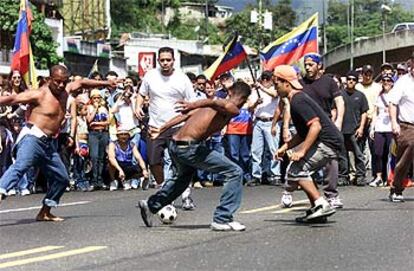 Chavistas (sin camisa) y opositores juegan al fútbol durante el bloqueo de una avenida de Caracas.