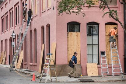 Tres hombres clausuran ventanas ante la llegada del huracán Matthew en Charleston.