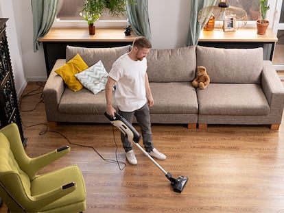 Un hombre pasando la aspiradora en el salón de su casa.