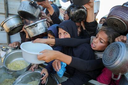 Los gazatíes se apresuran a recibir alimentos cocinados por una cocina benéfica en medio de una crisis de hambre.