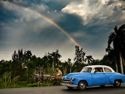 Un coche clásico estadounidense y un carro tirado por un caballo en una carretera de Cuba.