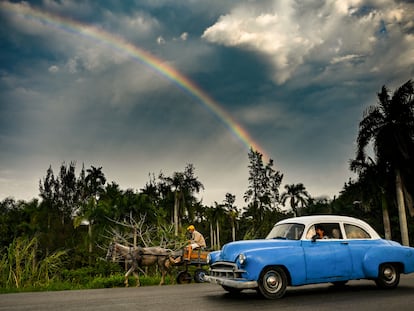 Un coche clásico estadounidense y un carro tirado por un caballo en una carretera de Cuba.