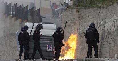 Agentes de policía se parapetan detrás de un contenedor, durante el enfrentamiento con los vecinos.