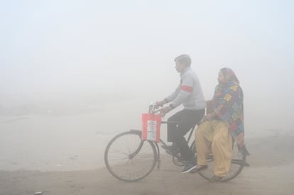 Una pareja circulan con una bicicleta entre una bruma de contaminación en Greater Noida (India), en noviembre de 2024.