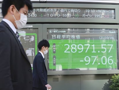 Dos personas caminan enfrente de un panel de un bróker japonés.