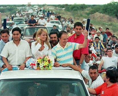 El expresidente de Argentina Carlos Menem saluda a la gente que lo aclama, desde un coche descubierto, acompañado por su esposa Cecilia Bolocco, a su llegada a su provincia natal La Rioja desde Buenos Aires. Menem regresó a su casa al día siguiente de ser absuelto de los cargos de tráfico de armas, tras ser autorizado a abandonar la casa donde se encontraba en arresto domiciliario, en noviembre de 2001.